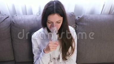 使用<strong>雾化</strong>器和吸入器进行治疗。 坐在沙发上的年轻女人通过吸入器面罩吸入。